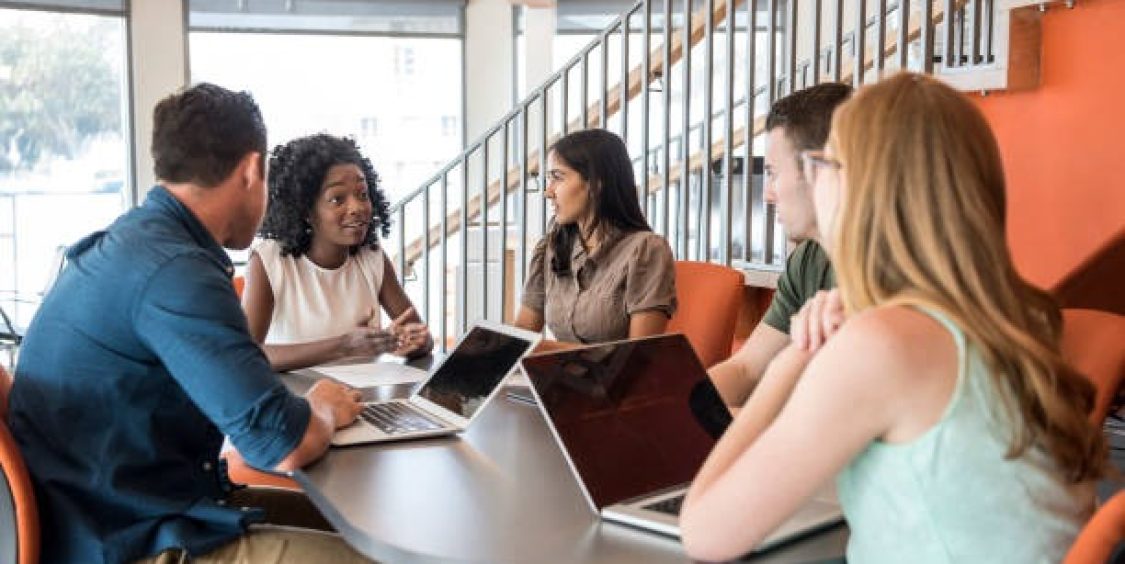 young-business-people-sitting-at-table-with-laptops-in-meeting
